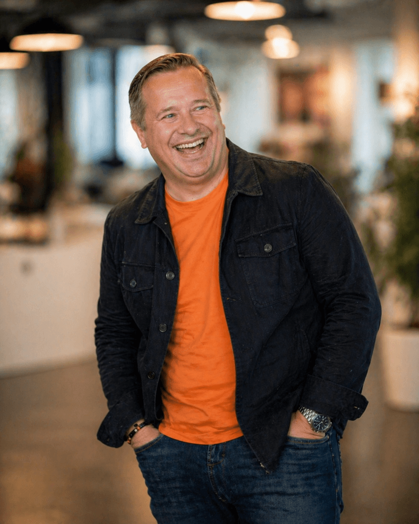 Niklas Jeppsson skrattar, i orange tröja och mörk jeansjacka.